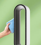 A modern white and black tower fan with a hand holding a blue microfiber cloth against its side, set against a soft green gradient background.