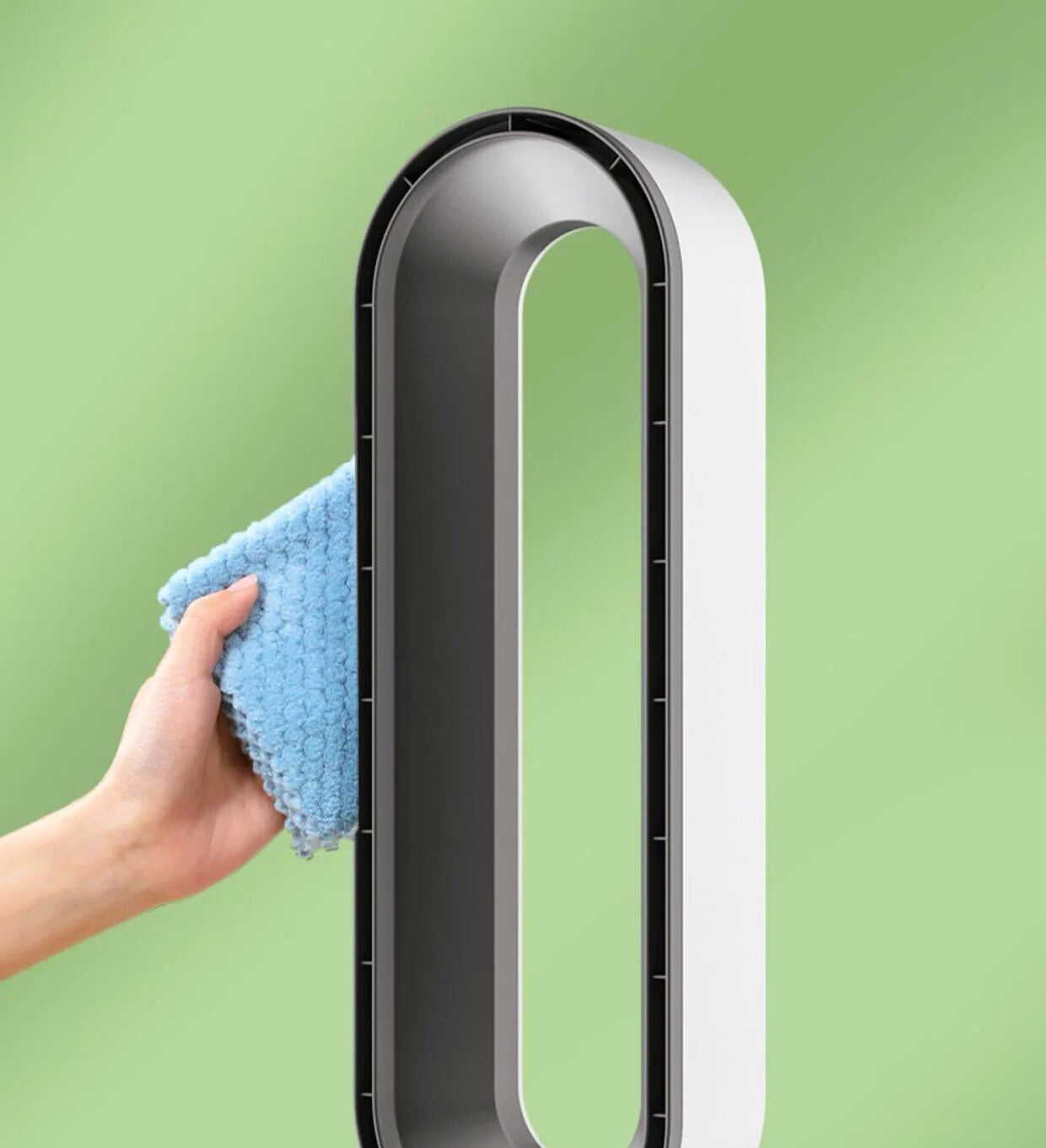 A modern white and black tower fan with a hand holding a blue microfiber cloth against its side, set against a soft green gradient background.