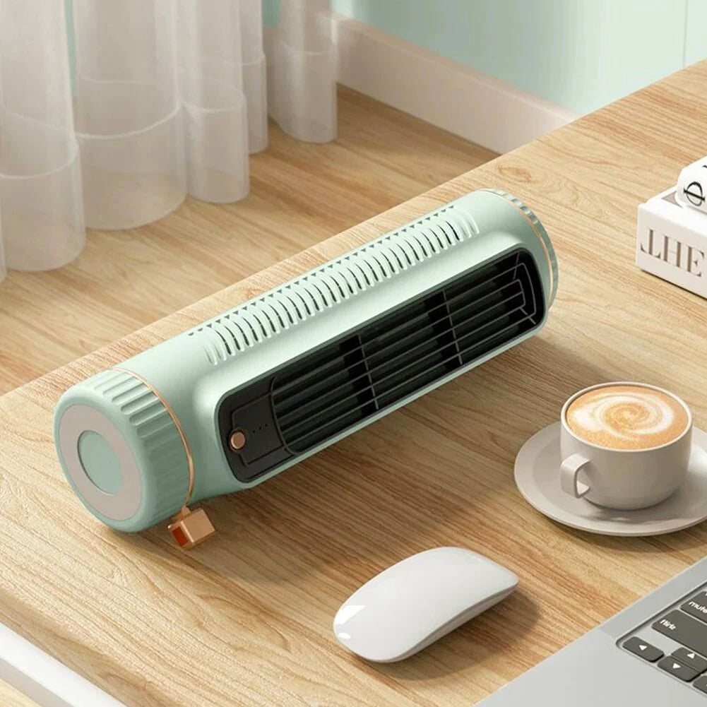 A compact, portable desk fan in a light mint green color with a black front grille, resting on a wooden desk next to a white computer mouse, a cup of latte macchiato, and a laptop.